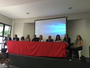 Foto: várias pessoas em um evento, sentadas junto a uma mesa de honra.