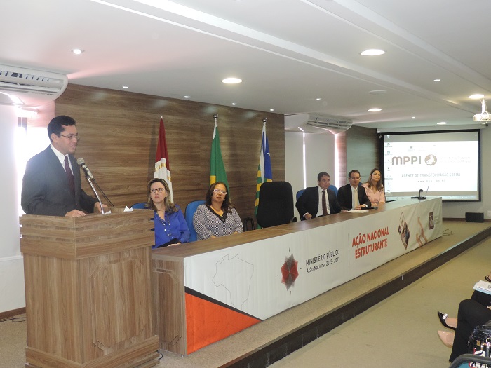 O Procurador-Geral de Justiça fala de pé junto à tribuna, com os membros da mesa de honra sentados em segundo plano.