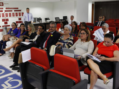 Pessoas sentadas nas cadeiras de um auditório. Do lado esquerdo, está a Promotora de Justiça Marlúcia Gomes Evaristo Almeida.