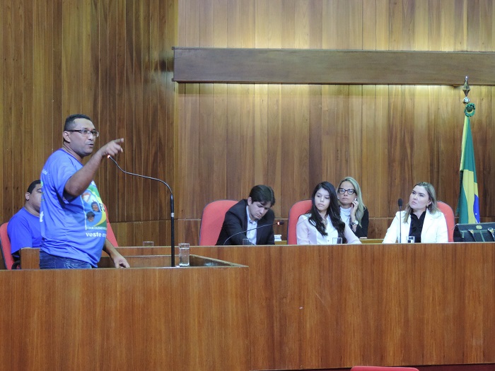 Homem discursando e outras pessoas assistindo 