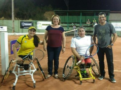 Pessoas sorrindo para foto em quadra de tênis. Desta duas são cadeirantes