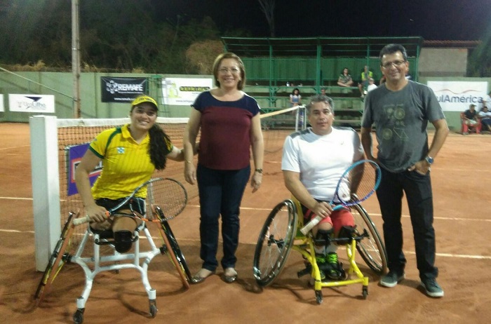 Pessoas sorrindo para foto em quadra de tênis. Desta duas são cadeirantes