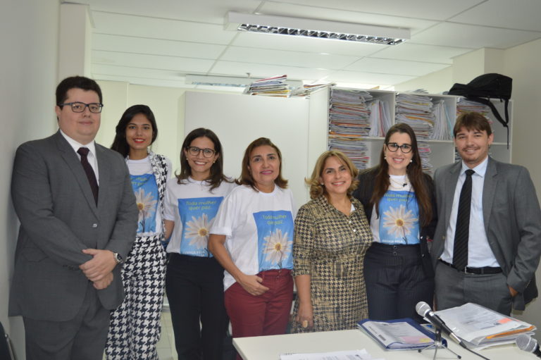 Equipe da Justiça pela Paz em Casa, posando de pé, sorrindo, em uma sala com vários armários preenchidos com processos.