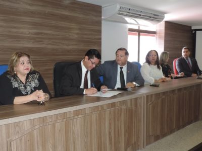 Procurador-Geral de Justiça assina documento na bancada do auditório.