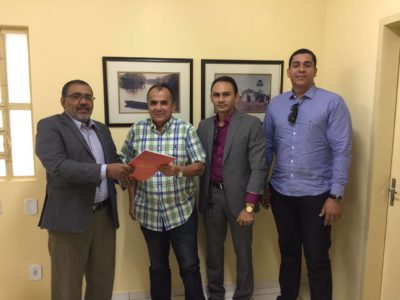 Promotor de Justiça de pé, entregando pasta com documentos ao prefeito de Piracuruca.