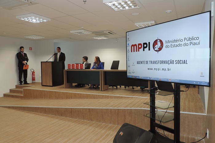 Pessoas sentadas e outra de pé discusando em uma tribuna