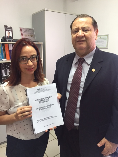 Promotora de Justiça entrega relatório nas mãos do Corregedor Geral, enquanto os dois posam para a câmera.