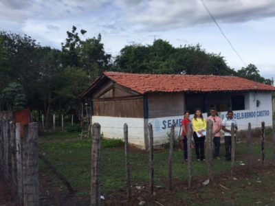 Equipe de inspeção na frente de uma escola cercada por mato.