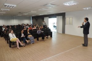Pessoas sentadas assistindo palestra e um homem de pé falando