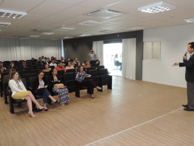Pessoas sentadas assistindo palestra e um homem de pé falando