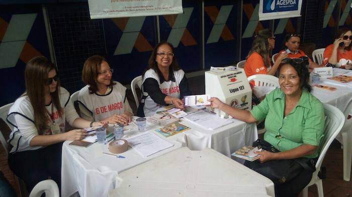 Ouvidora do MPPI entrega folheto informativo para cidadã durante atendimento em praça pública.