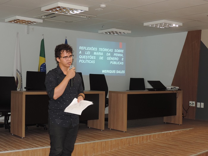Homem de pé segurando documentos e falando ao microfone