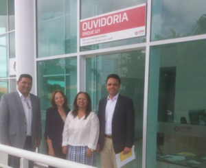 Imagem com quatro pessoas de pé. Ao fundo, uma placa em que lê