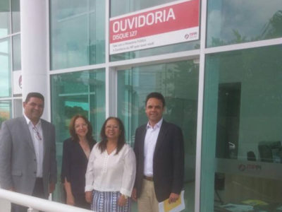 Imagem com quatro pessoas de pé. Ao fundo, uma placa em que lê