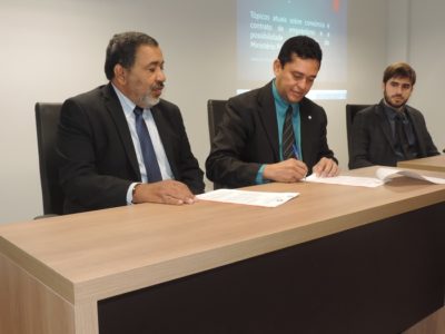 Três pessoas sentados e dos três assinando documento