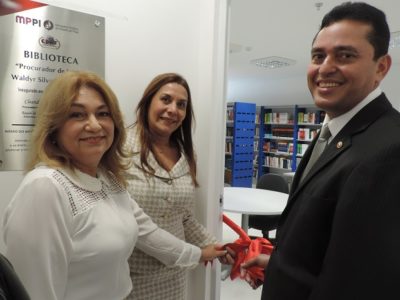 Três pessoas segurando uma fita e sorrindo para foto