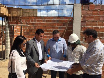 Pessoas analisam uma planta de construção, em pé, em um canteiro de obras.