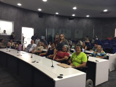 A Promotora de Justiça Marlúcia Evaristo de pé, em meio a pessoas em cadeiras de rodas, no plenário da Câmara Municipal.