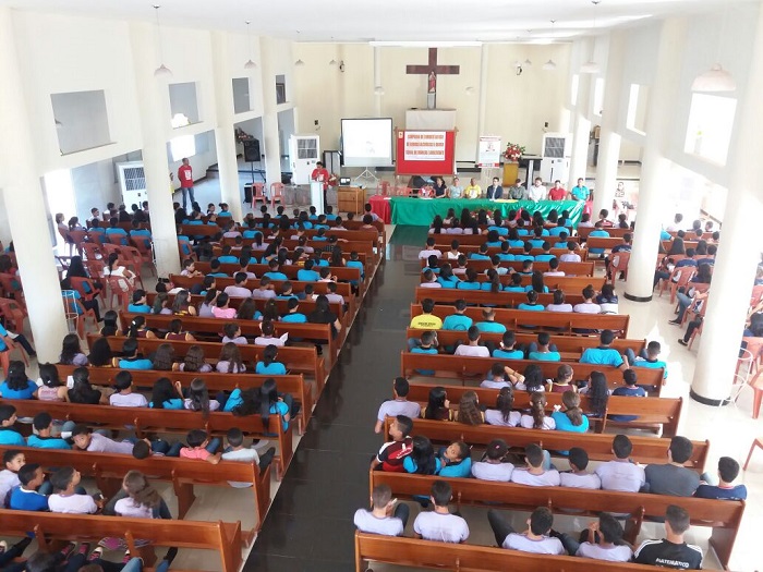 Pessoas sentadas dentro de uma igreja observando um homem de pé falando 
