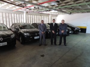 Três pessoas de pé e carros atrás