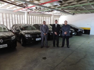 Três pessoas de pé e carros atrás