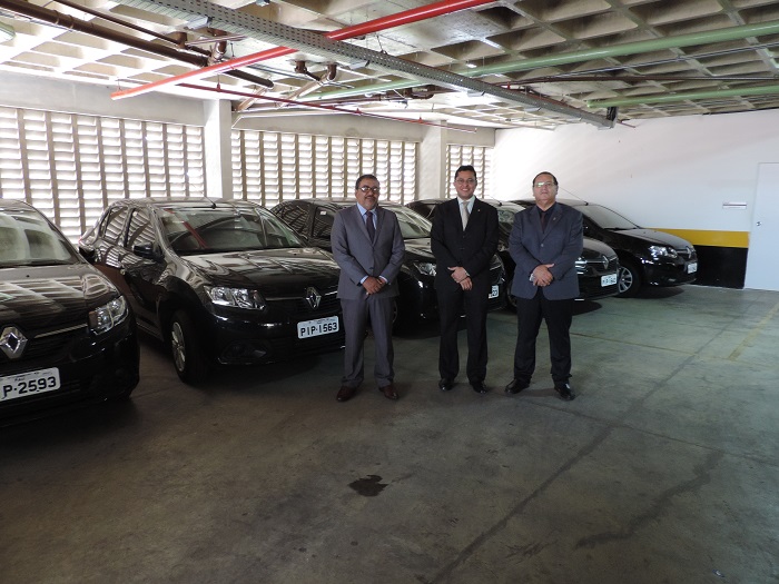 Três pessoas de pé e carros atrás