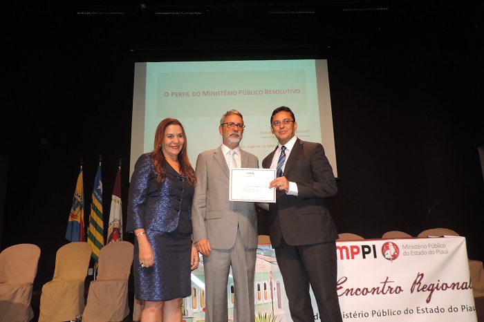 Três pessoas de pé, um segura um certificando entregando o mesmo para o outro 