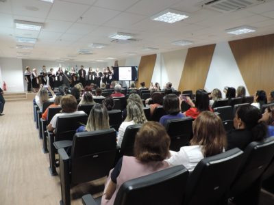 Pessoas sentadas num auditório assistindo apresentação do coral