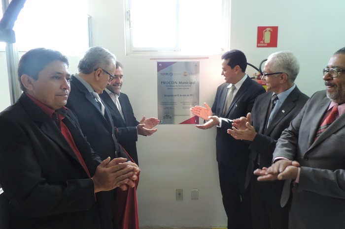 Homens de pé batendo palmas após decerrar a placa da inauguração do Procon