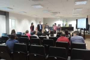 Quatro pessoas de pé enquanto as demais estão sentadas