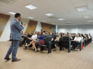 Pessoas sentadas e um homem de pé com microfone na mão