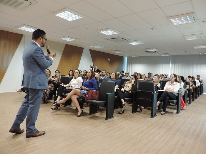 Pessoas sentadas e um homem de pé com microfone na mão