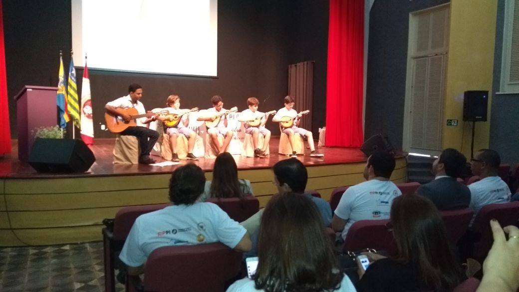 Crianças tocam bandolins em um palco.