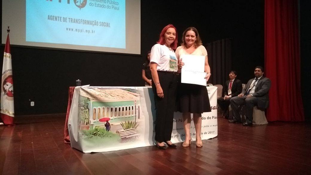 Em um palco, palestrante recebe certificado de participação.