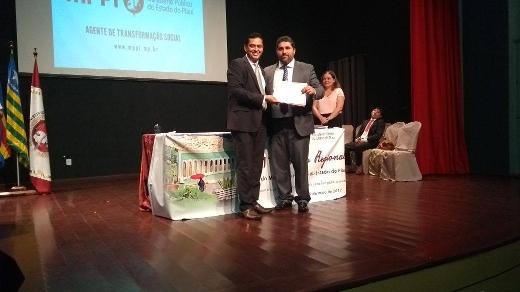 Em um palco, palestrante recebe certificado de participação.