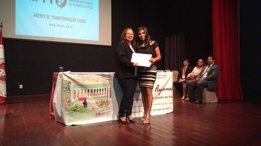 Em um palco, palestrante recebe certificado de participação.
