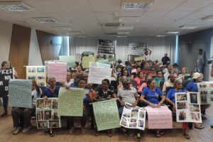 Vários idosos no auditório do Ministério Público, com cartazes de protesto