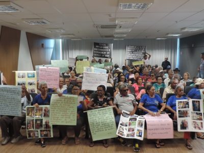 Vários idosos no auditório do Ministério Público, com cartazes de protesto