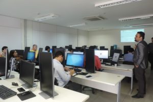 Pessoas sentadas em sala de aula observando um homem