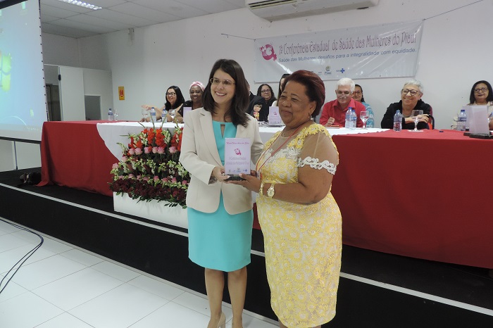 Duas mulheres, uma entrega uma placa de homenagem para a outra 
