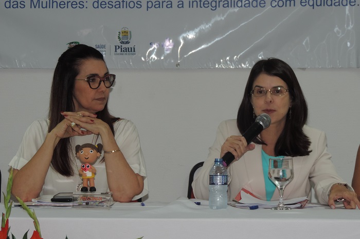 Duas mulheres, uma delas está microfone na mão e a outra observar enquanto fala
