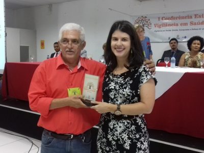 Duas pessoas de pé um das quais entrega uma placa para outro