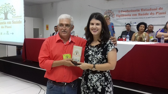 Duas pessoas de pé um das quais entrega uma placa para outro