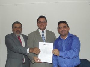 Três homens de pé sorrindo e segurando um documento