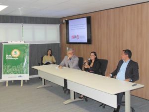 Quatro pessoas sentadas, dos quais uma mulher com microfone