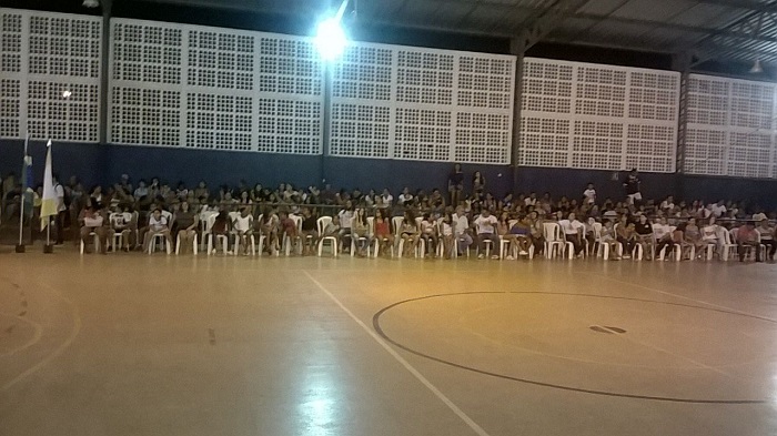 Pessoas sentada em ginásio enquanto assistem uma palestra 