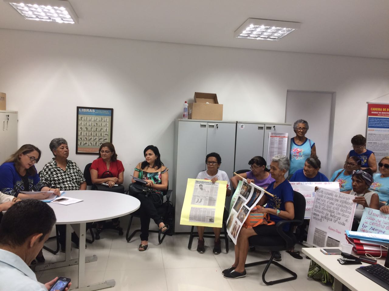 Sala lotada de pessoas, com cartazes de protesto.