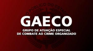 Imagem: fundo vermelho, com o brasão do Ministério Público. Em primeiro plano, está escrito: GAECO - Grupo de Atuação Especial de Combate ao Crime Organizado.