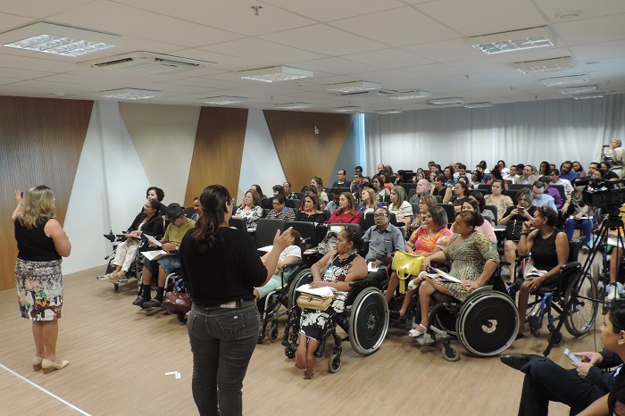 Auditório lotado. Palestre e intérprete de LIBRAS em primeiro plano.