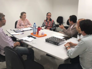 Pessoas sentadas em reunião, em torno de uma mesa retangular.